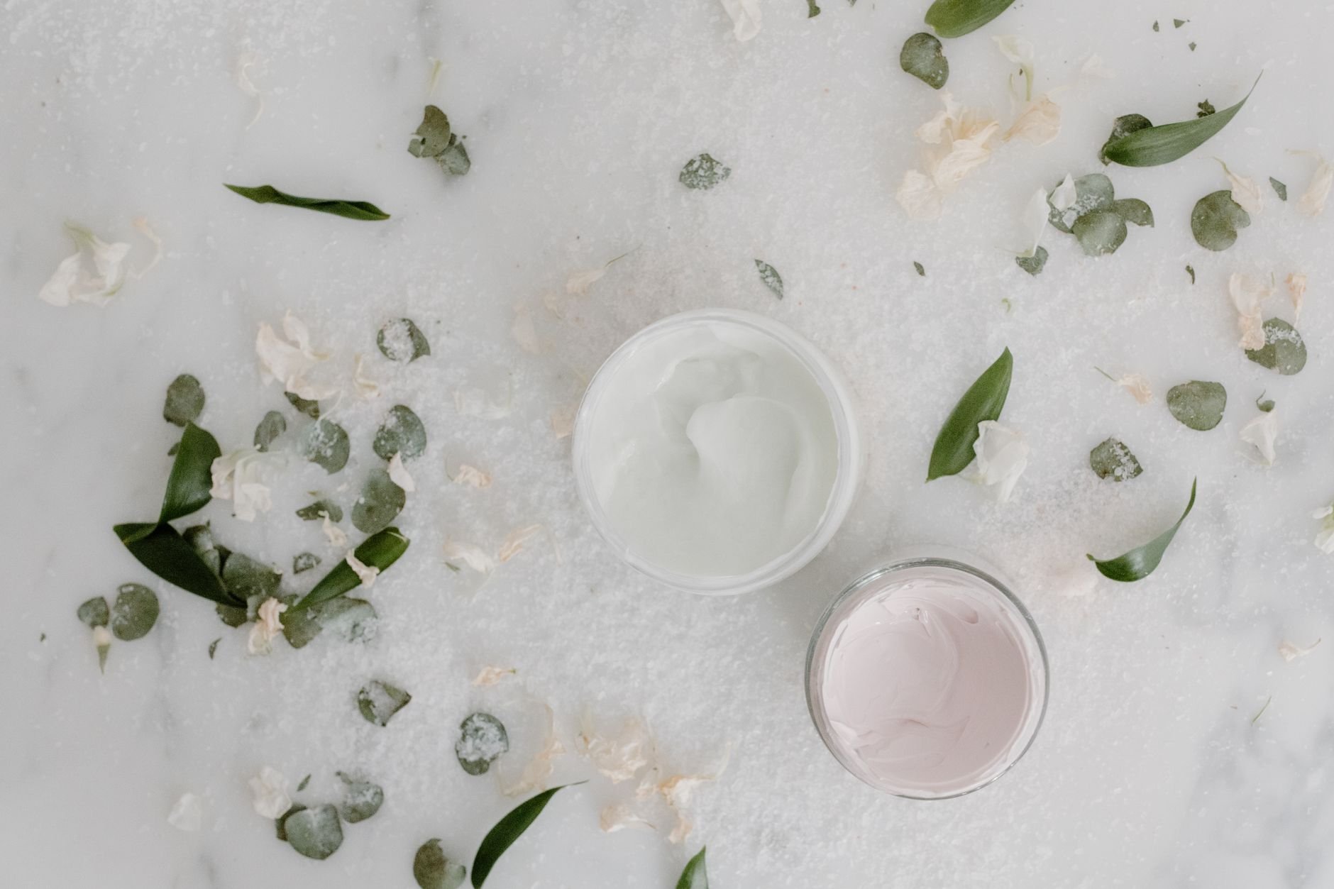 Flat lay of natural botanical ingredients and cream jars surrounded by leaves and petals